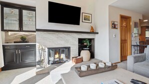 Una sala moderna con chimenea, un televisor de pantalla plana montado encima y una zona de estar acogedora con una mesa de centro.