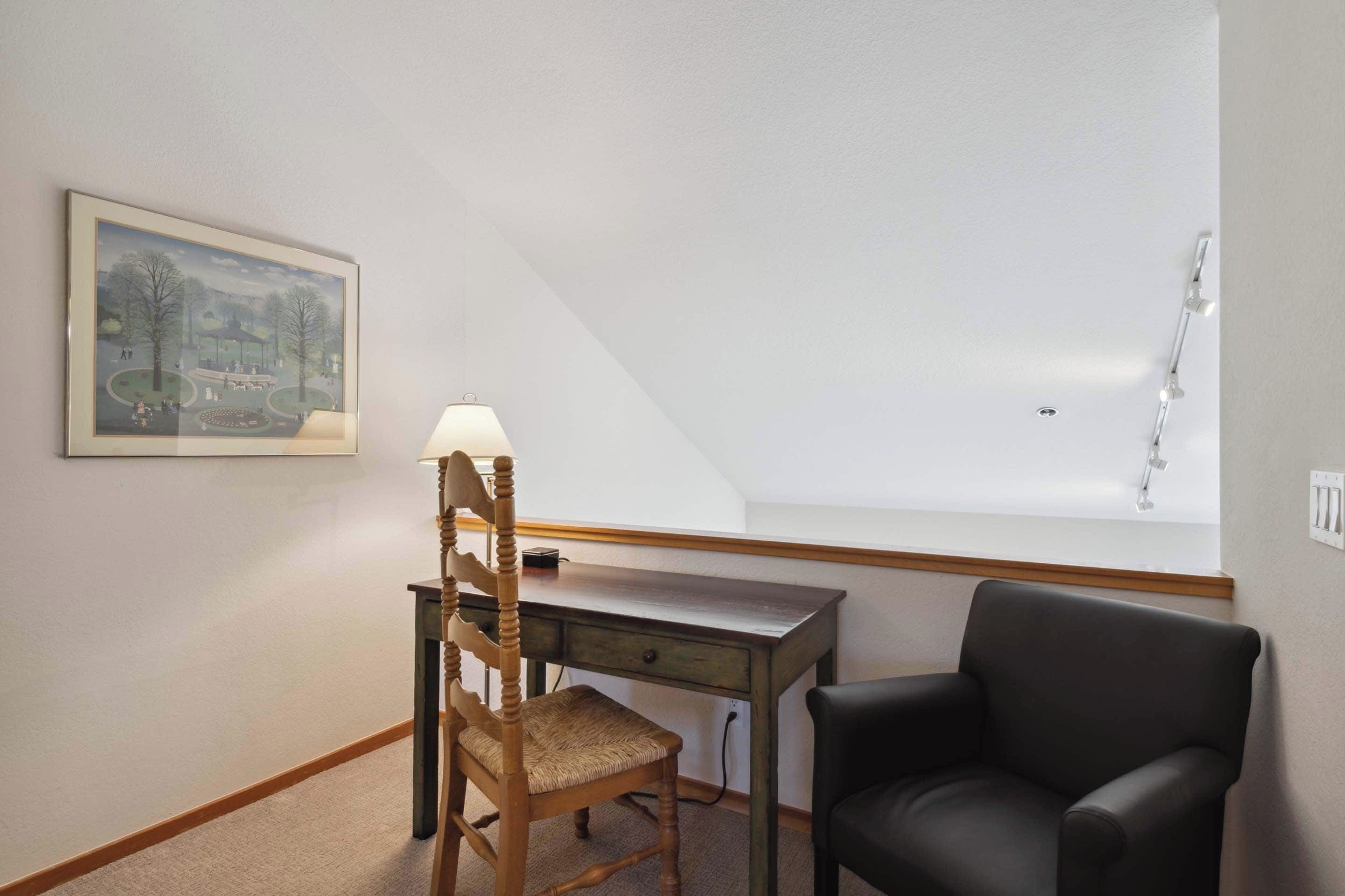 A room with a desk, a chair, a lamp, and a painting on the wall.