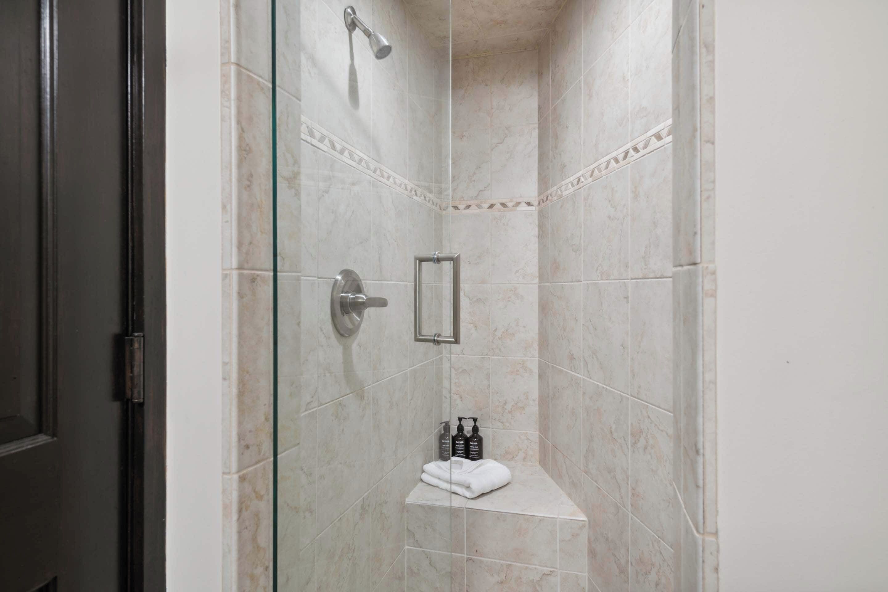 Une douche fermée par des parois en verre, dotée d’un pommeau de douche à main, d’un porte-serviettes et d’une étagère pour les articles de toilette.