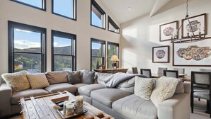 A modern living room with a sectional sofa, a wooden coffee table, and a dining area with chairs.