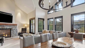 A spacious living room with a fireplace, comfortable seating, a large wooden dining table, and large windows offering a scenic view.