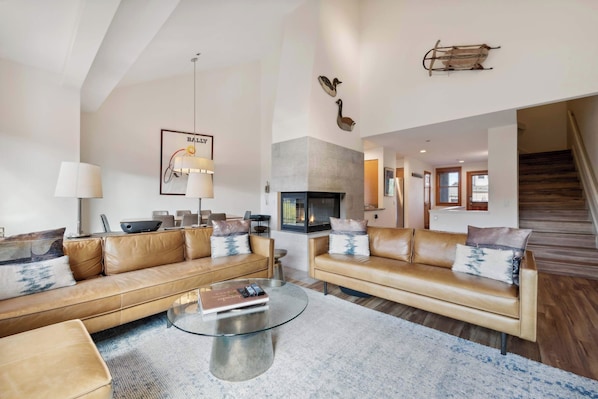 A spacious living room with leather sofas, a glass coffee table, and a fireplace.