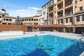 A swimming pool with a wooden deck and a stone building in the background.