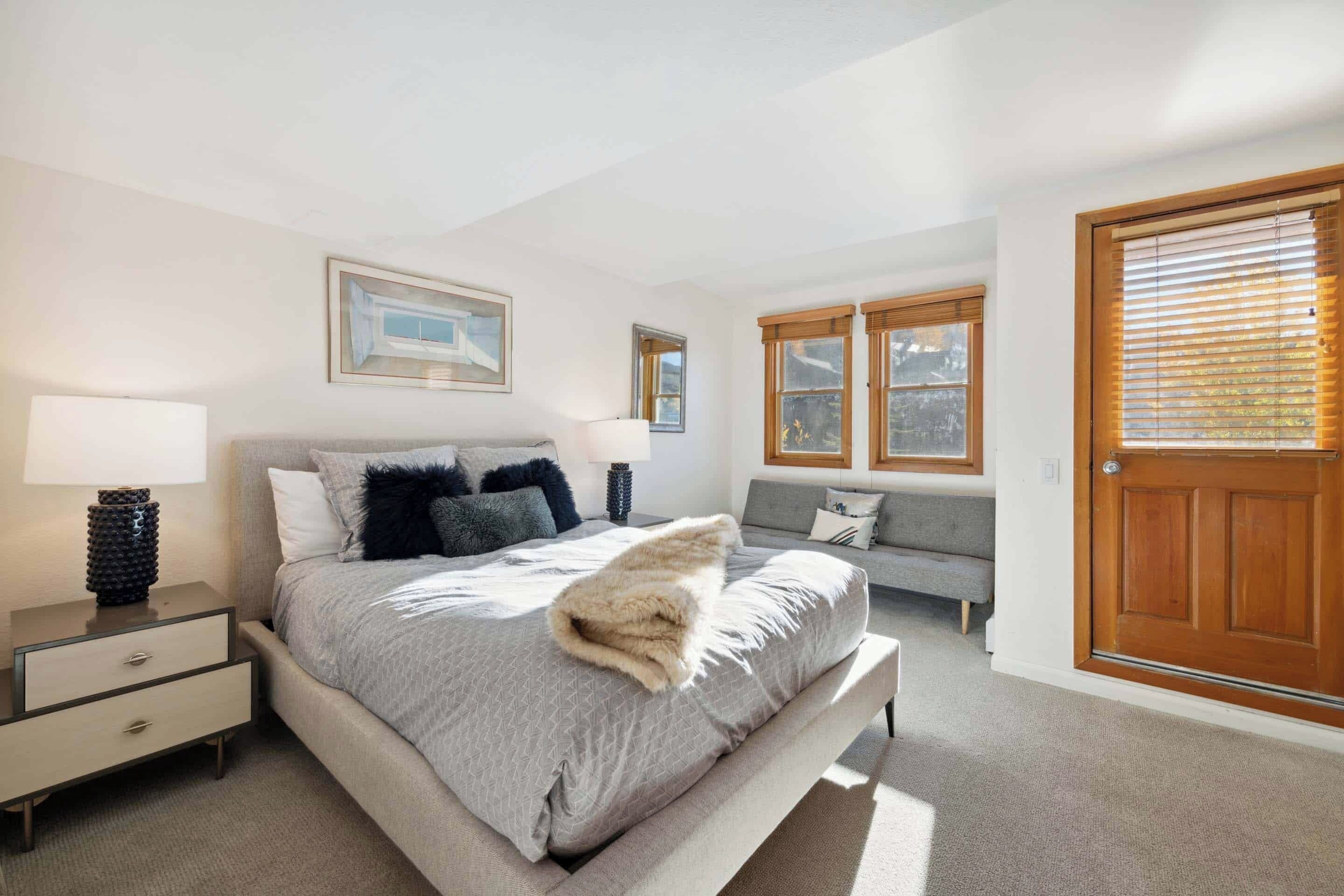 A bedroom with a bed, bedside tables, a bench, and a door.