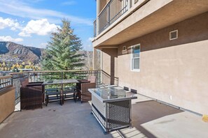 A balcony with wicker furniture, a glass-top table, and a view of mountains.