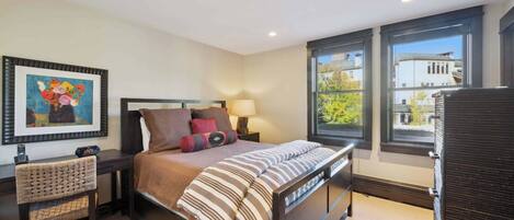 A bedroom with a bed, bedside tables, a chair, a lamp, and a window with a view of buildings.
