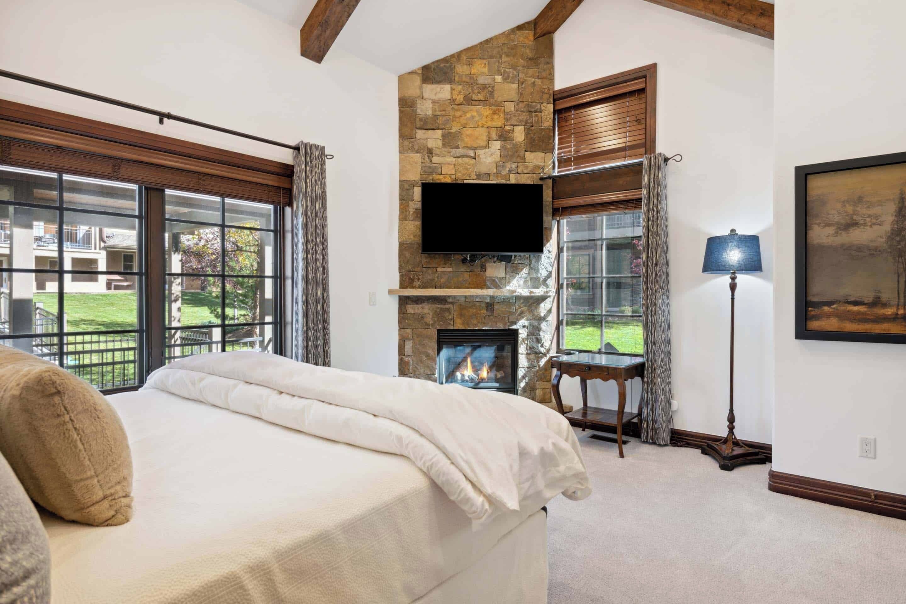 Un dormitorio con chimenea de piedra, televisor de pantalla plana y ventanas grandes.