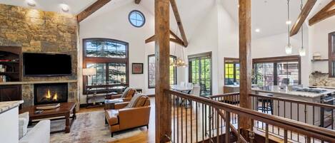 A spacious living area with a stone fireplace, wooden beams, and a view of the outdoors.