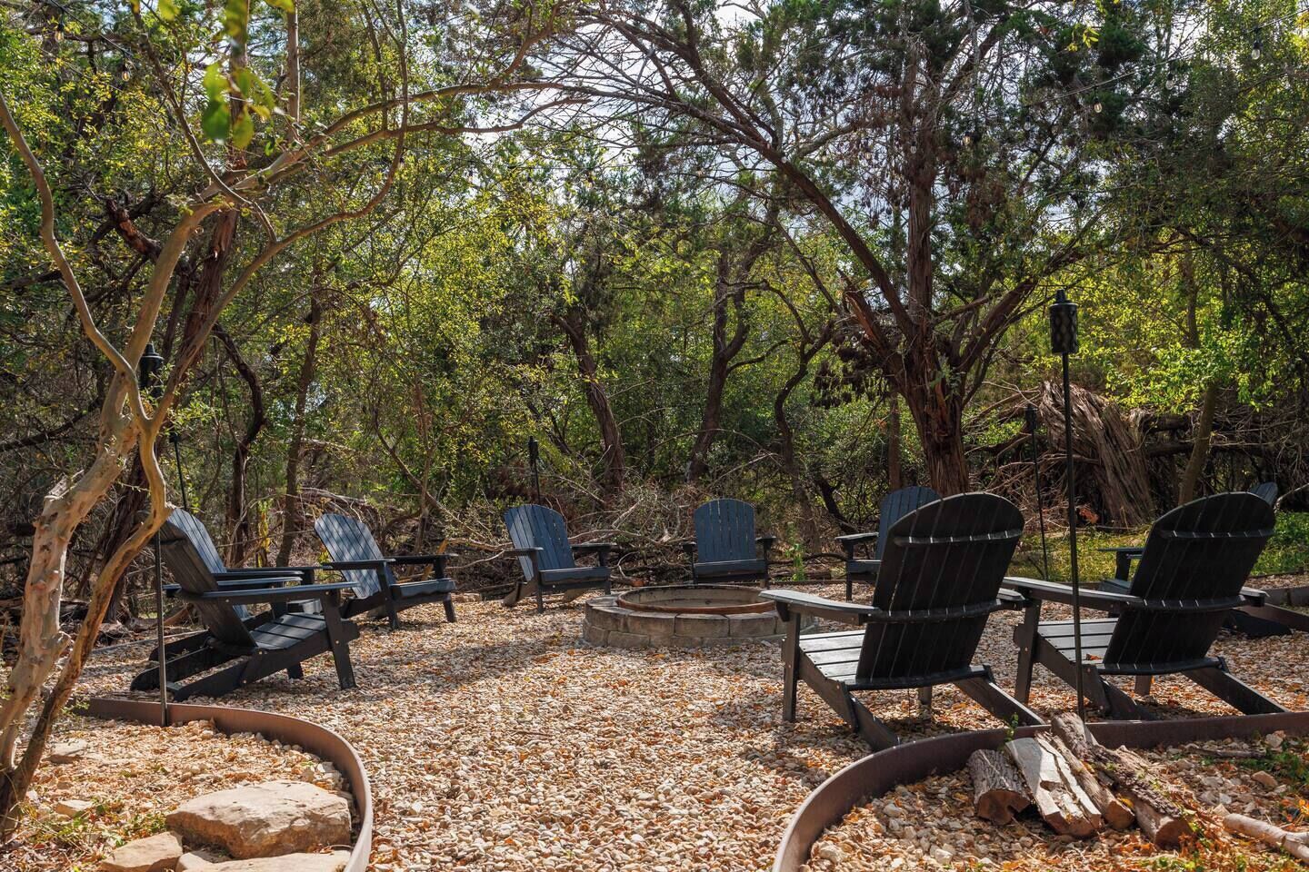 An outdoor seating area with Adirondack chairs and a fire pit surrounded by trees.