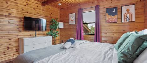 Quarto de cabana de madeira com uma cama, uma TV, uma planta e obras de arte nas paredes.