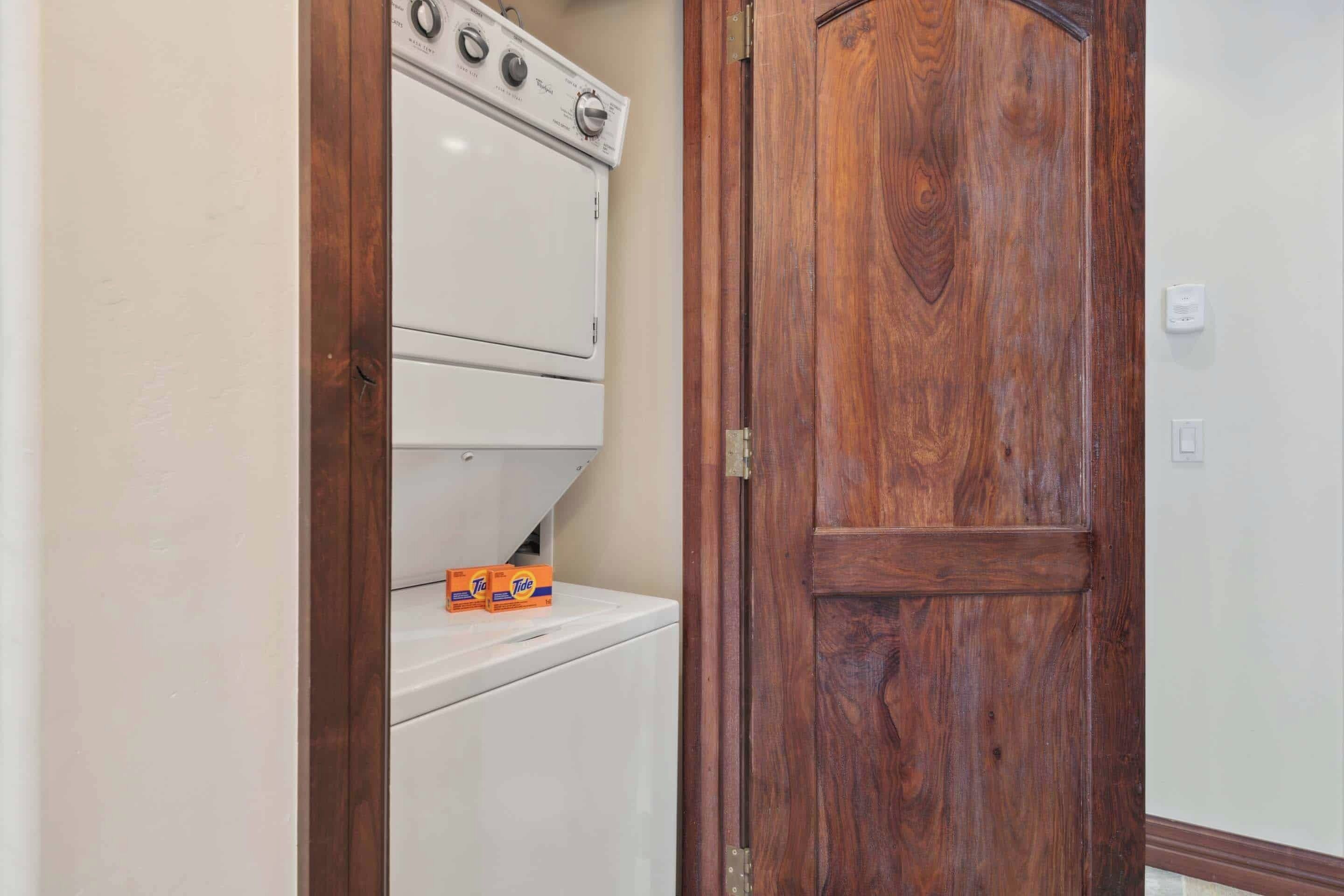 Une buanderie avec des machines à laver et des sèche-linge superposés, une porte en bois et un mur blanc.