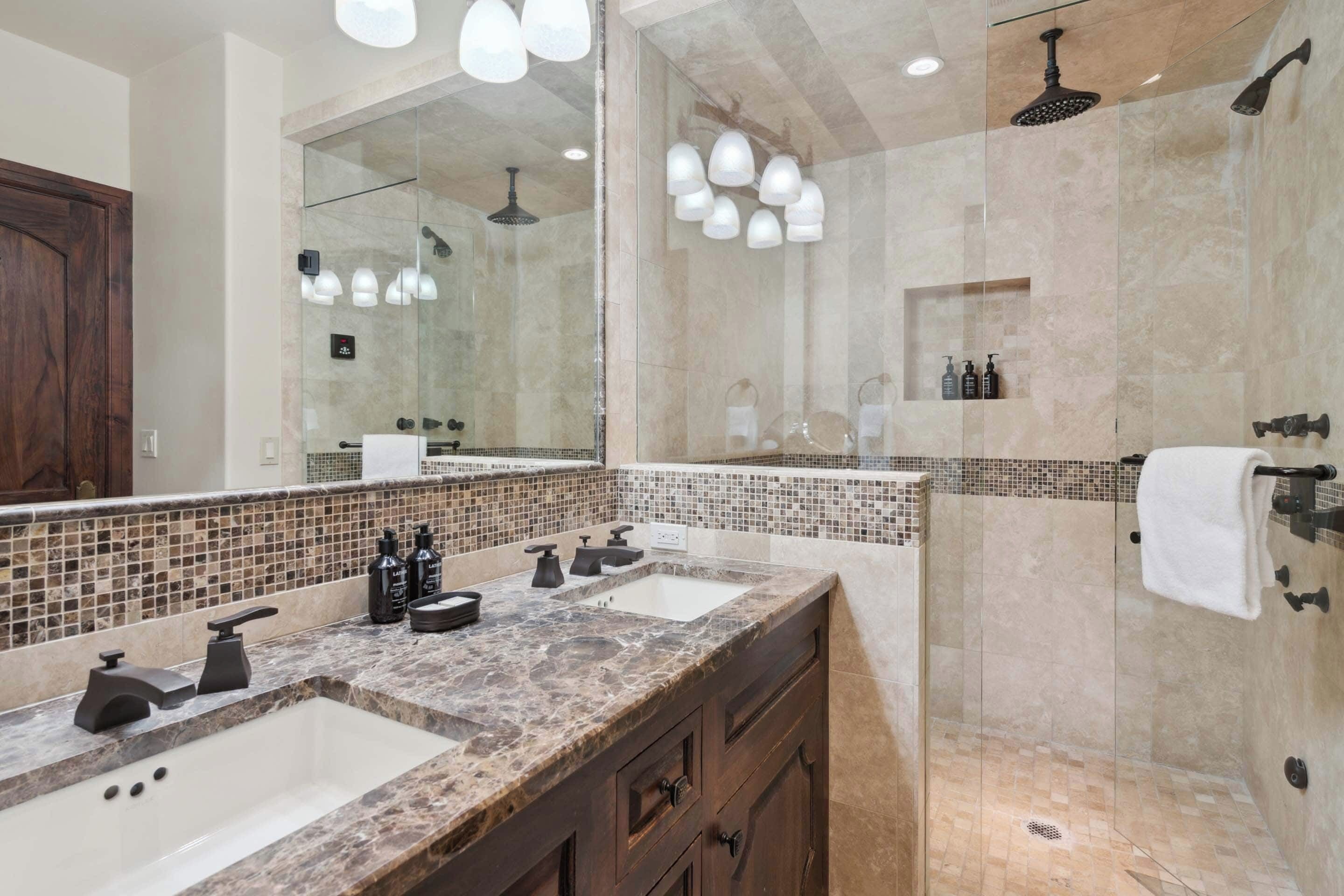 A modern bathroom with two sinks, a glass-enclosed shower, and a large mirror.