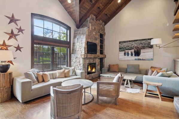 A cozy living room with a stone fireplace, large windows, and comfortable seating.