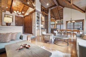 A spacious living area with a high ceiling, wooden beams, a fireplace, and a dining area with a table and chairs.