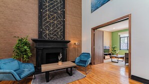 Een moderne woonkamer met een open haard, twee blauwe fauteuils, een houten salontafel en een potplant.