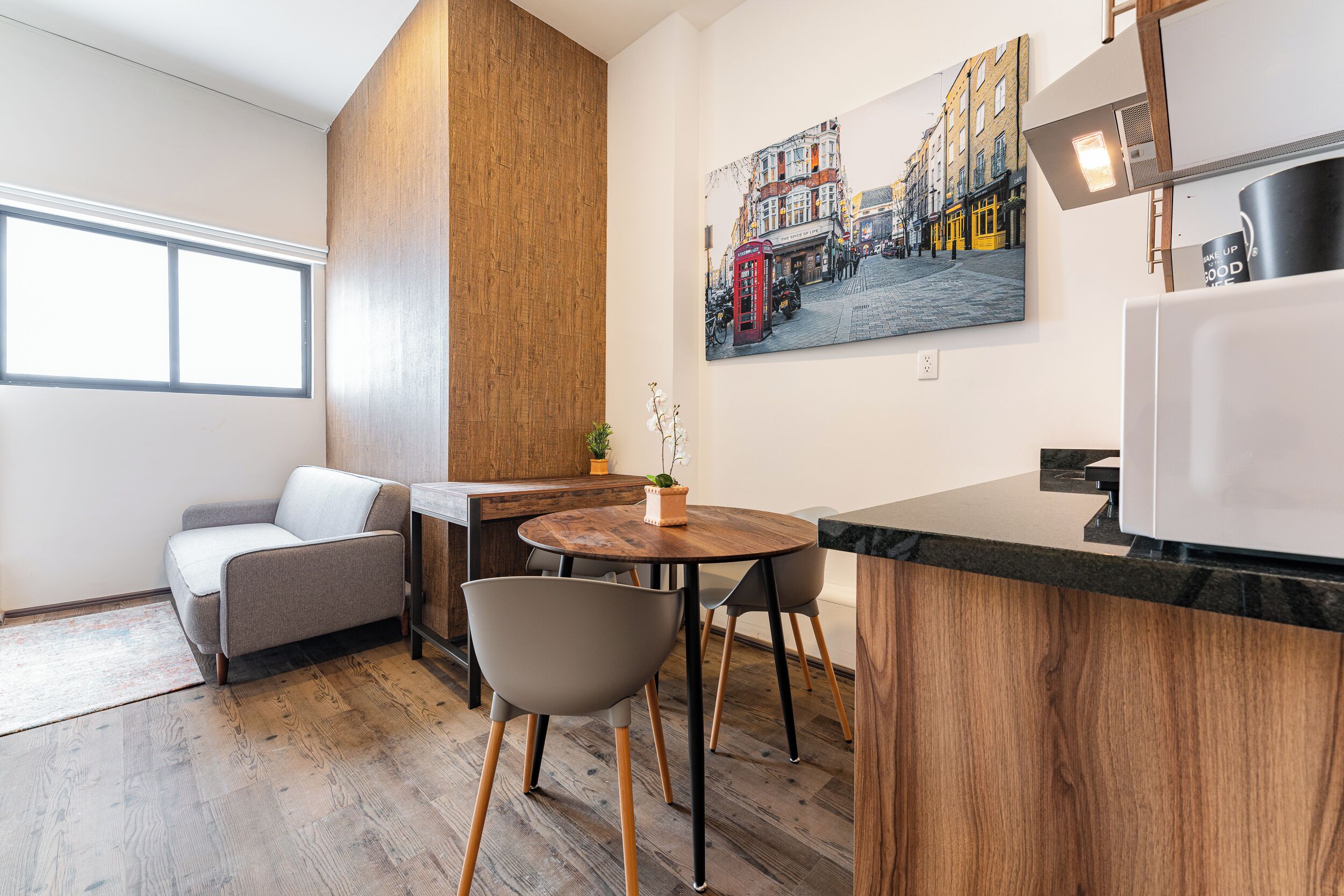A modern kitchen with a wooden accent wall, a dining area with a round table and chairs, and a large cityscape painting on the wall.