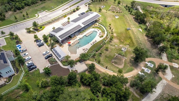 An aerial view of a commercial building with a swimming pool, parking area, and surrounding greenery. - Relaxing 3BR Retreat Community Pool Gym (Manor)