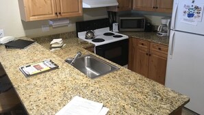 A kitchen with wooden cabinets, a granite countertop, a stainless steel sink, a stove, a microwave, and a refrigerator.