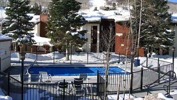 A pool area with a fenced deck, surrounded by snow-covered trees and buildings.