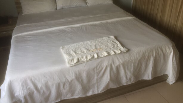 A large bed with white linens, a wooden headboard, and a small white towel on the bed. - Clinclia Hotels (Ibadan)
