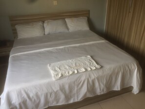 Un grande letto con lenzuola bianche, una testata in legno e un piccolo asciugamano bianco sopra il letto.