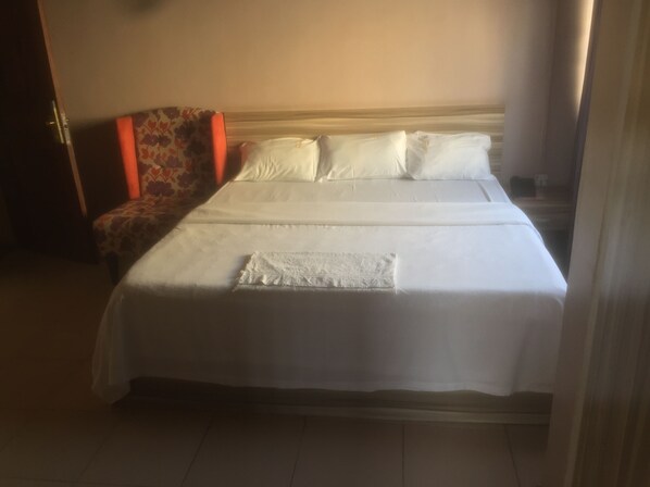 A double bed with white linens, a floral chair, and a bedside table with a lamp.