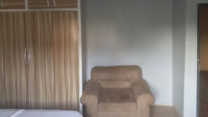 A bedroom with a bed, a wooden wardrobe, and a brown armchair. - Clinclia Hotels (Ibadan)