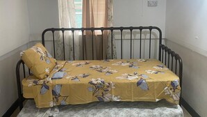 A single bed with a floral bedspread, a window with sheer curtains, and a wall-mounted fan. - Beautiful Cozy Private Studio with WiFi in Charming Salisbury (Salisbury)
