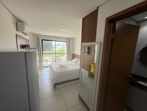 Habitación de hotel pequeña con cama, escritorio, espejo y vista al balcón exterior.