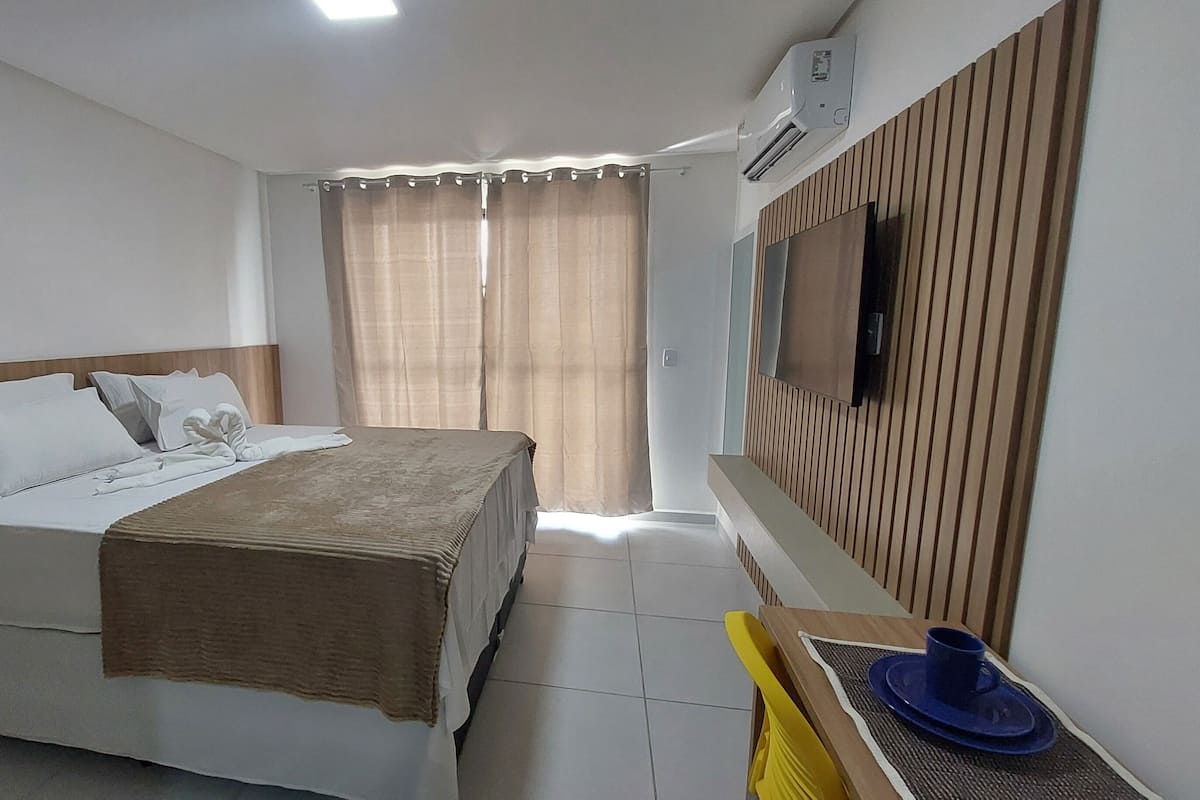 A hotel room with a bed, a TV mounted on the wall, and a window with curtains.