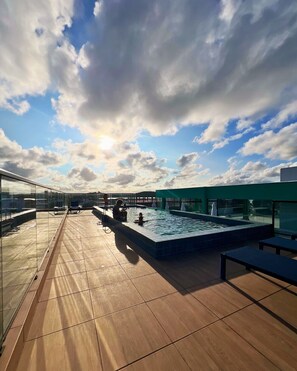 A rooftop pool area with a glass balustrade, a pool with a tiled deck, and a clear sky with clouds. - Varandas do Porto Use Flats (Ipojuca)
