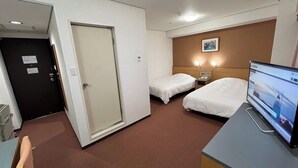 Ein Hotelzimmer mit zwei Einzelbetten, einem Schreibtisch mit Computer, einer Tür und einem kleinen Nachttisch mit Lampe.