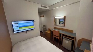 Ein Hotelzimmer mit einem Bett, einem Schreibtisch, einem Stuhl, einer kleinen Kühlbox, einem an der Wand montierten Fernseher und einem Spiegel über dem Schreibtisch.