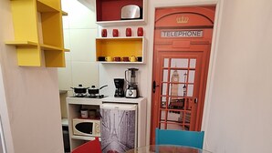 Et spiseområde med et glasbord, røde og blå stole, en rød dør med teksten "TELEPHONE" og en gul reol.