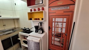 Et køkken med komfur, gryder, en blender og en kaffemaskine. Der er en hylde med kopper, og en dør med teksten "TELEPHONE".