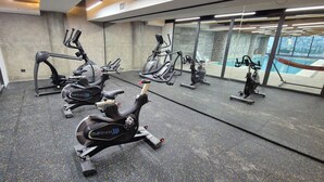 A gym with multiple stationary bikes, a mirrored wall, and a view of an outdoor swimming pool. - Hotel Diego de Almagro La Serena Express (La Serena)