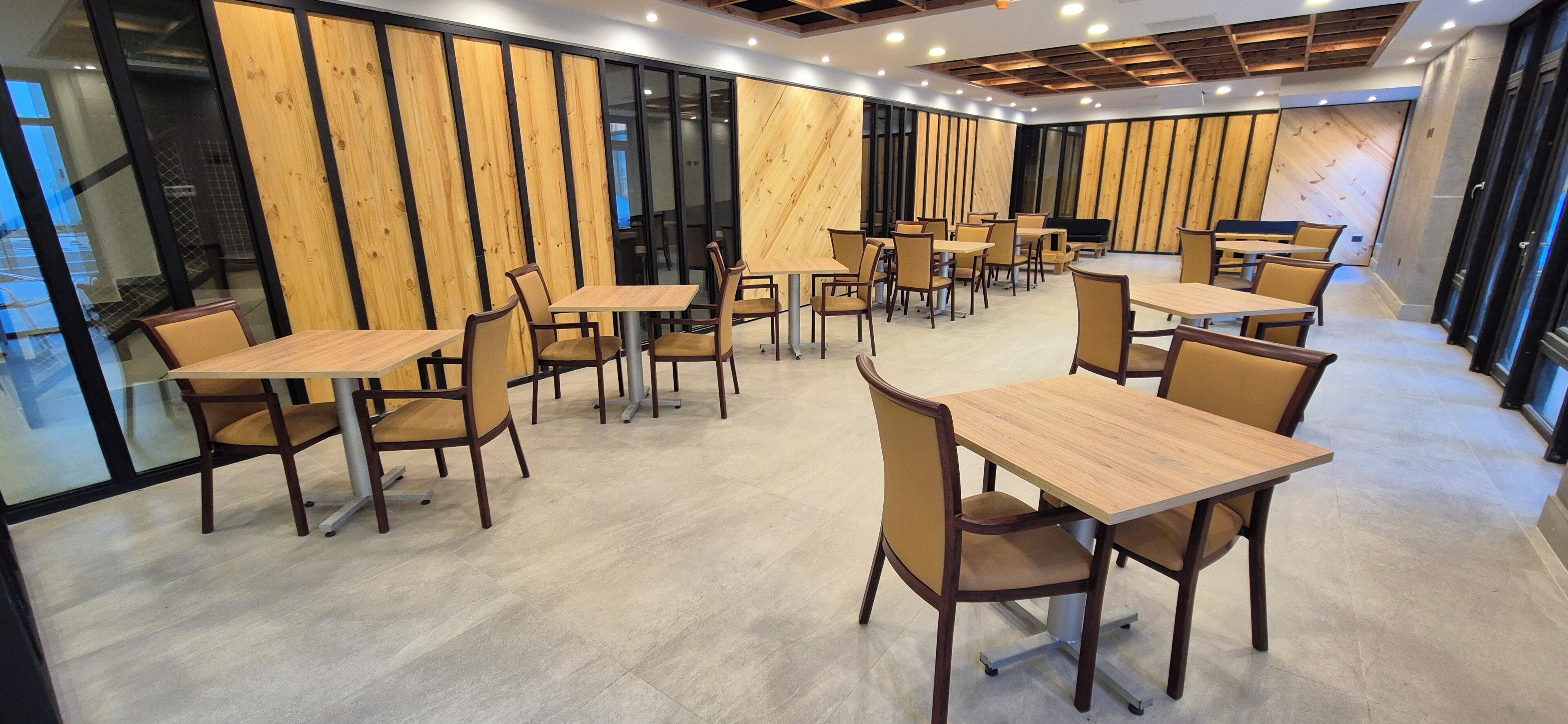 Un comedor moderno con paneles de madera, varias mesas y sillas, y ventanas amplias.