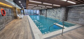 Une piscine intérieure avec un sol carrelé, une bouée de sauvetage et un mur en pierre.