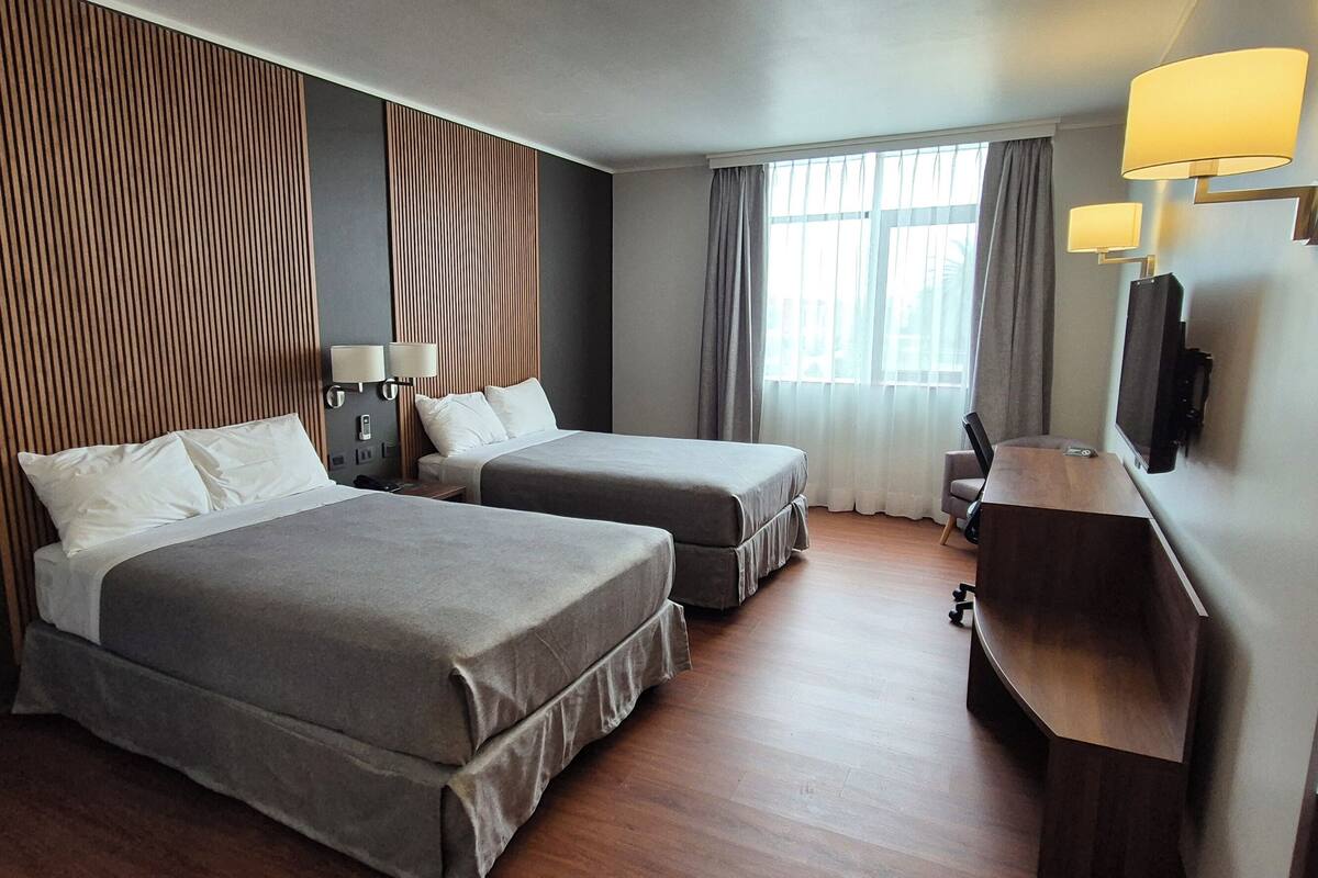 Une chambre d’hôtel avec deux lits, une tête de lit en bois, une télévision et un bureau.