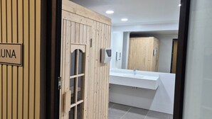 A sauna room with a wooden door labeled "SAUNA" and a modern bathroom with a sink and mirror. - Hotel Diego de Almagro La Serena Express (La Serena)