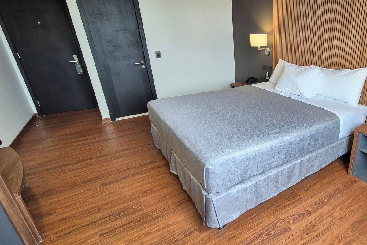 Une chambre d’hôtel avec un lit, des tables de chevet, une chaise et un plancher en bois.