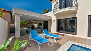 Ein moderner Poolbereich im Freien mit Liegestühlen und einer sichtbaren Küchenzeile durch eine offene Terrasse.