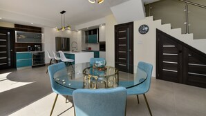 Eine moderne Küche mit integrierten Geräten, eine Essecke mit Glastisch und blauen Stühlen sowie eine Treppe mit Metallgeländer.
