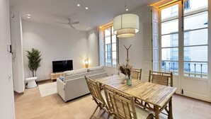 A modern living room with a sofa, TV, dining table, chairs, and a large window with a view. - Zarzuela (Málaga)