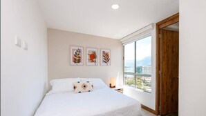 Un dormitorio con cama, mesita de noche, ventana con vistas y tres cuadros colgados en la pared.
