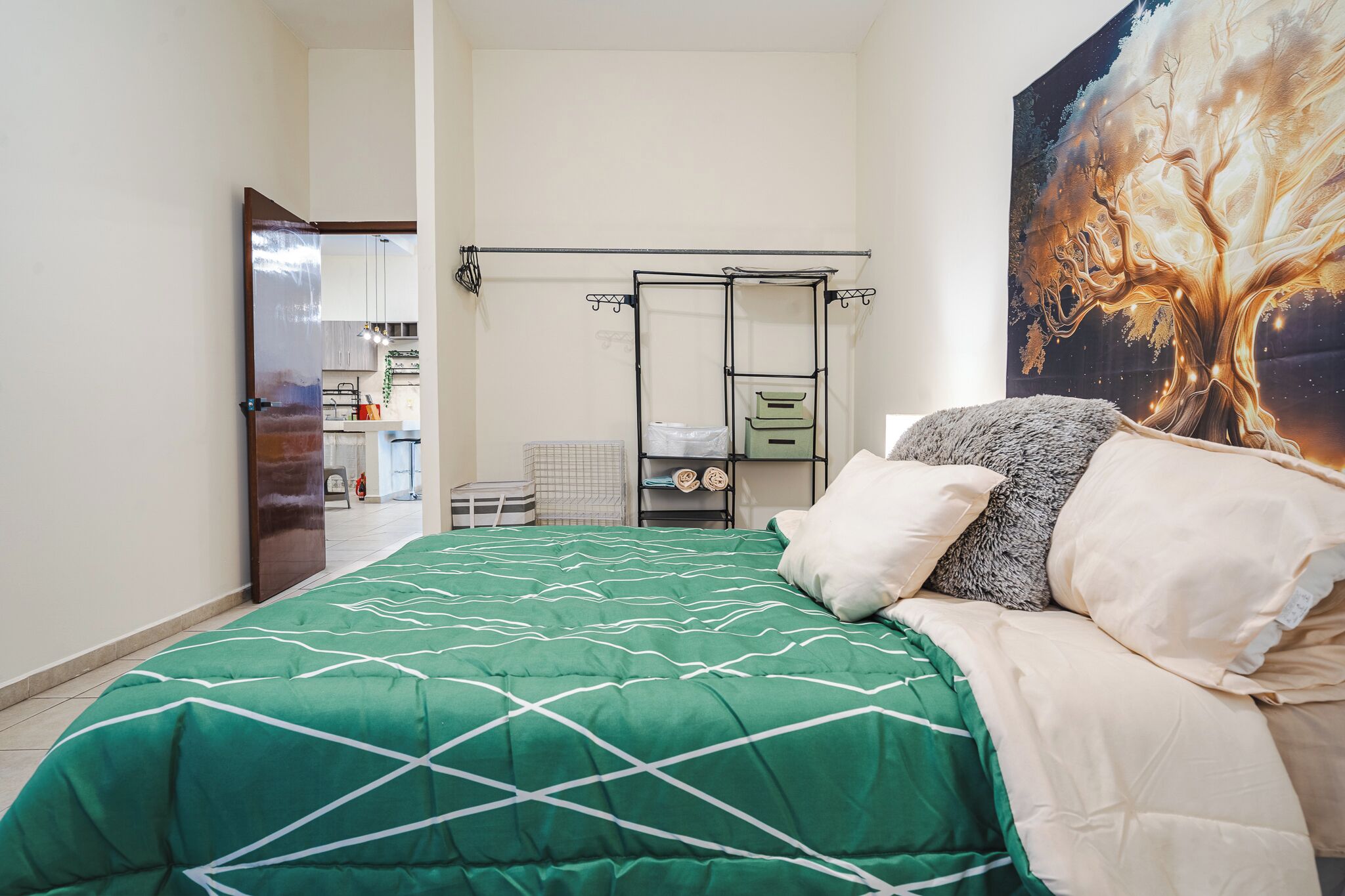 Une chambre avec une couvre-lit verte, un grand tableau au mur et une armoire avec un miroir.