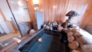 A stone hot tub surrounded by rocks, wooden walls, and a tiled floor. - Hotel Alpha-One Yonezawa (Yonezawa)