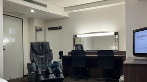 Quarto de hotel com uma cama, uma cadeira de massagem, uma mesa com computador e um espelho grande.