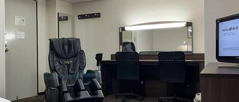 A hotel room with a bed, a massage chair, a desk with a computer, and a large mirror.