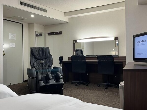 A hotel room with a bed, a massage chair, a desk with a computer, and a large mirror.